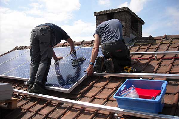 Two installers fitting a solar panel to rails on a tiled roof